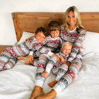 Happy family of four wearing matching Christmas pyjamas, sitting by a decorated Christmas tree and smiling, cozy holiday pajamas nightwear for men, women, and kids.
