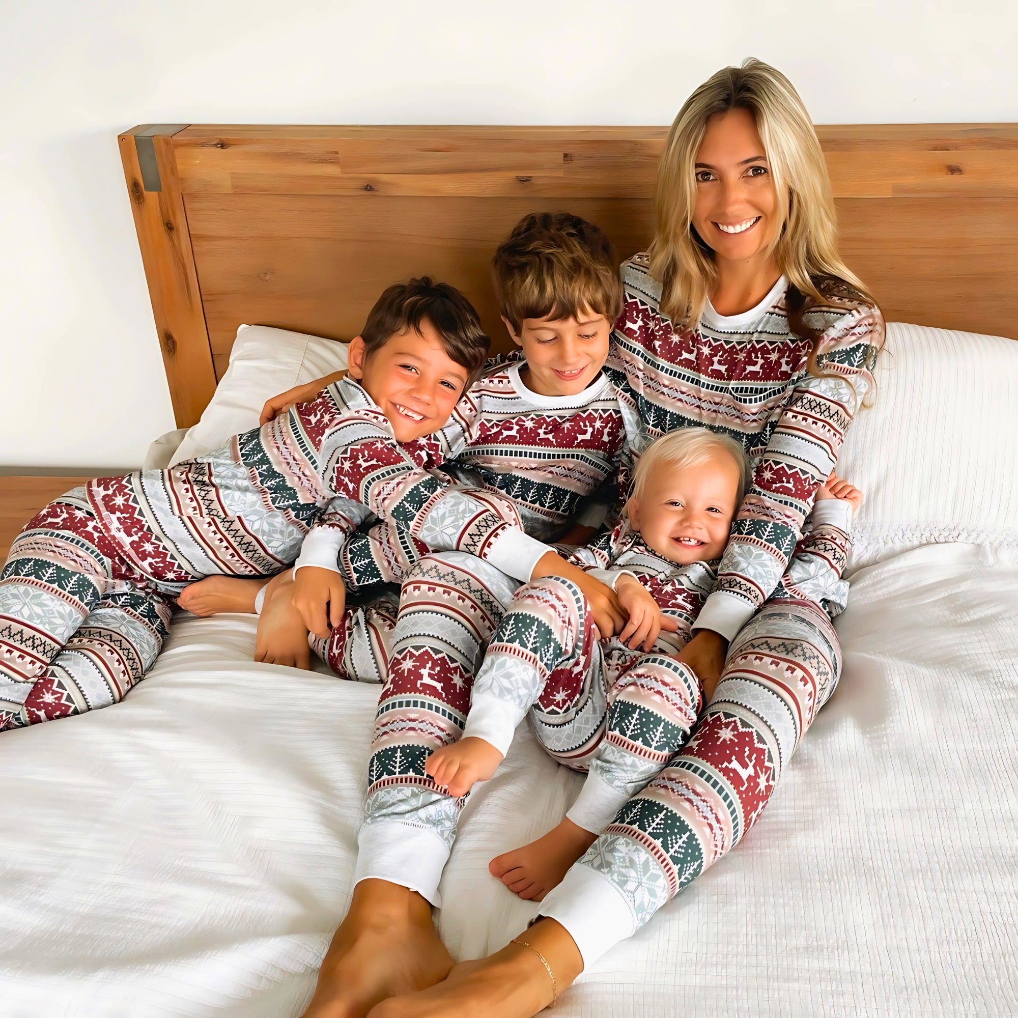Happy family of four wearing matching Christmas pyjamas, sitting by a decorated Christmas tree and smiling, cozy holiday pajamas nightwear for men, women, and kids.