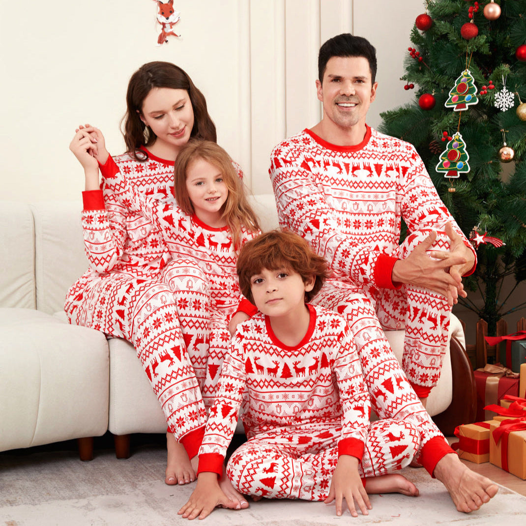 Family in matching red and white pajamas sitting on a couch with a Christmas tree in the background.