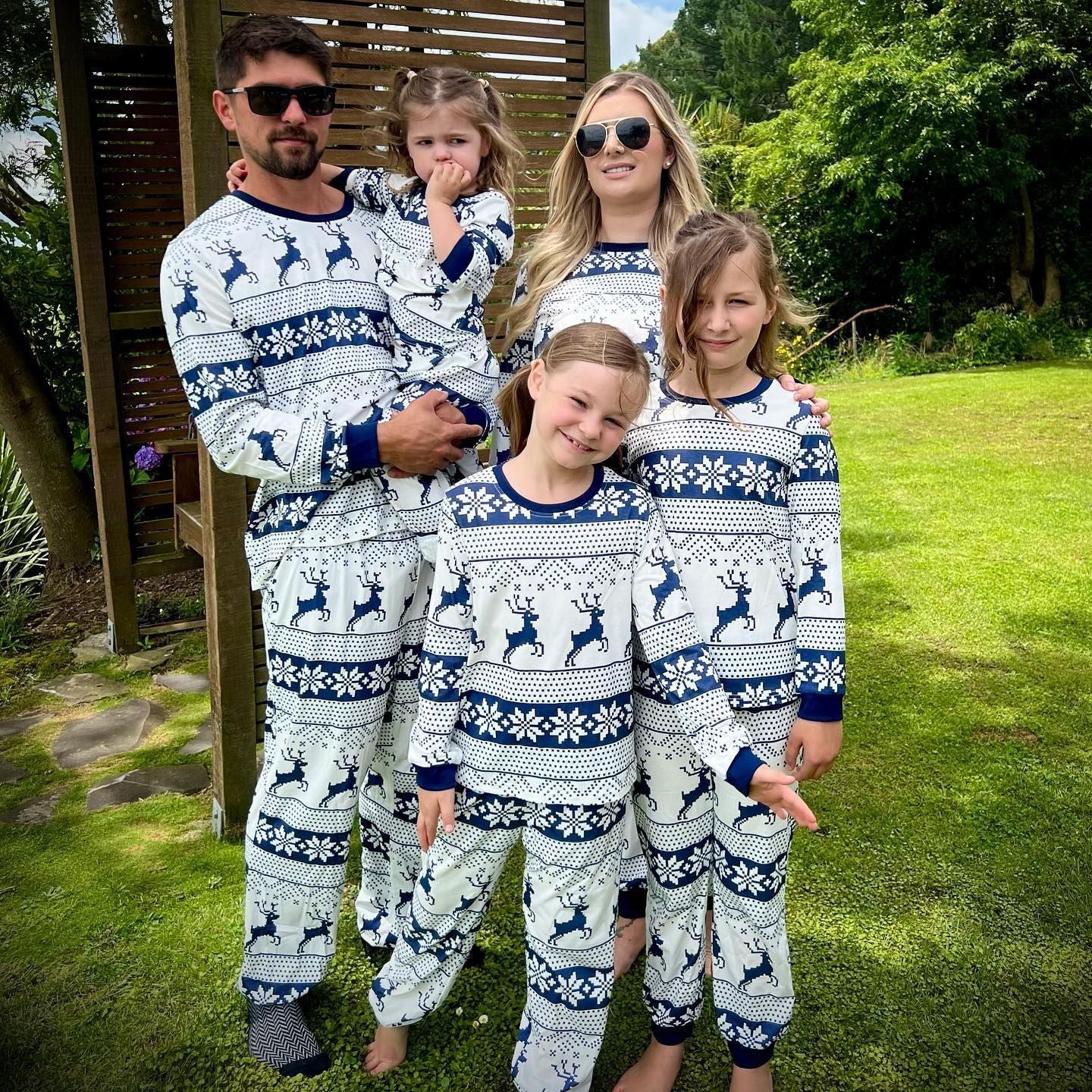 Family of five wearing matching blue and white pajamas with reindeer pattern outdoors.