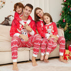 Family in matching red pajamas with white patterns sitting on a couch in a festive living room.