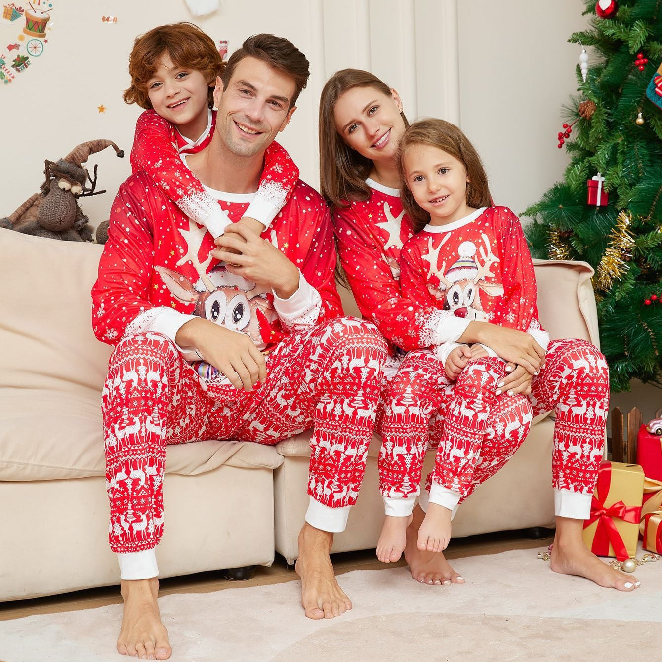 Family in matching red pajamas with white patterns sitting on a couch in a festive living room.