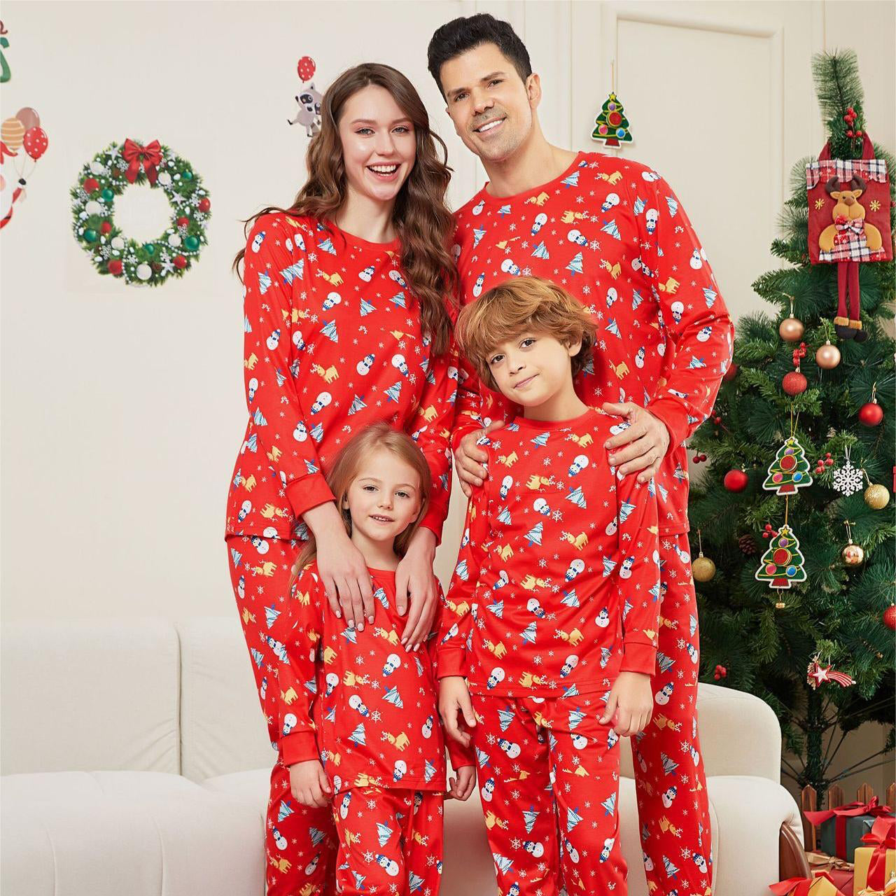 Family of four wearing red Christmas pajamas in a living room decorated for the holidays.